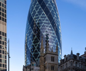 A modern skyscraper with a distinctive curved, glass facade, known as "The Gherkin," towers over historic buildings in a city skyline. The sky is clear and blue.