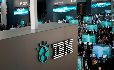 A busy conference hall with large IBM branding displays promoting Media & Entertainment and Retail solutions. Attendees gather around booths showcasing various technologies and solutions.